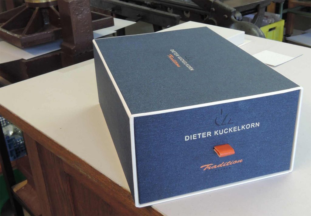 Geschlossener Karton für handgefertigtes Schuhwerk von Dieter Kuckelkorn, mit geprägtem Firmenlogo, Ledergriff und farbig abgesetzten Kanten.