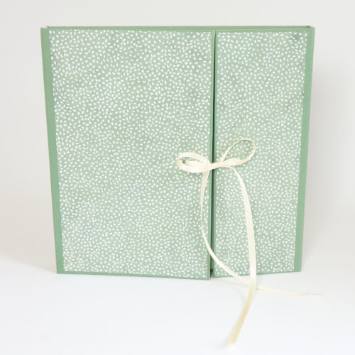 Kleines Fotoalbum mit Verschlussklappen und Schleife. Grüner Bucheinband, Cover aus Naturpapier mit Reiskornmotiv.