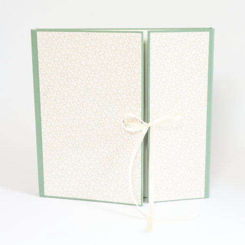 Kleines quadratisches Fotoalbum mit grünem Bezugspapier und Dekor aus weiss bedrucktem Naturpapier. Geteilter Klappdeckel und Verschluss aus weissem Satinschleifenband.