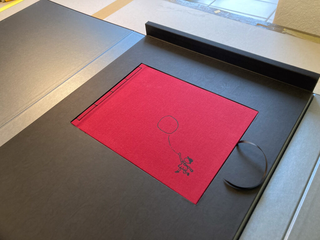 Kinderbuch Till Lindemann "Lieber Fritz nimm meine Hand" mit rotem Leineneinband und schwarzem Prägemotiv eines Kindes mit Luftballon, in der geöffneten Buchkassette des Gedichtbandes "Am Sonntag muss ich sterben"