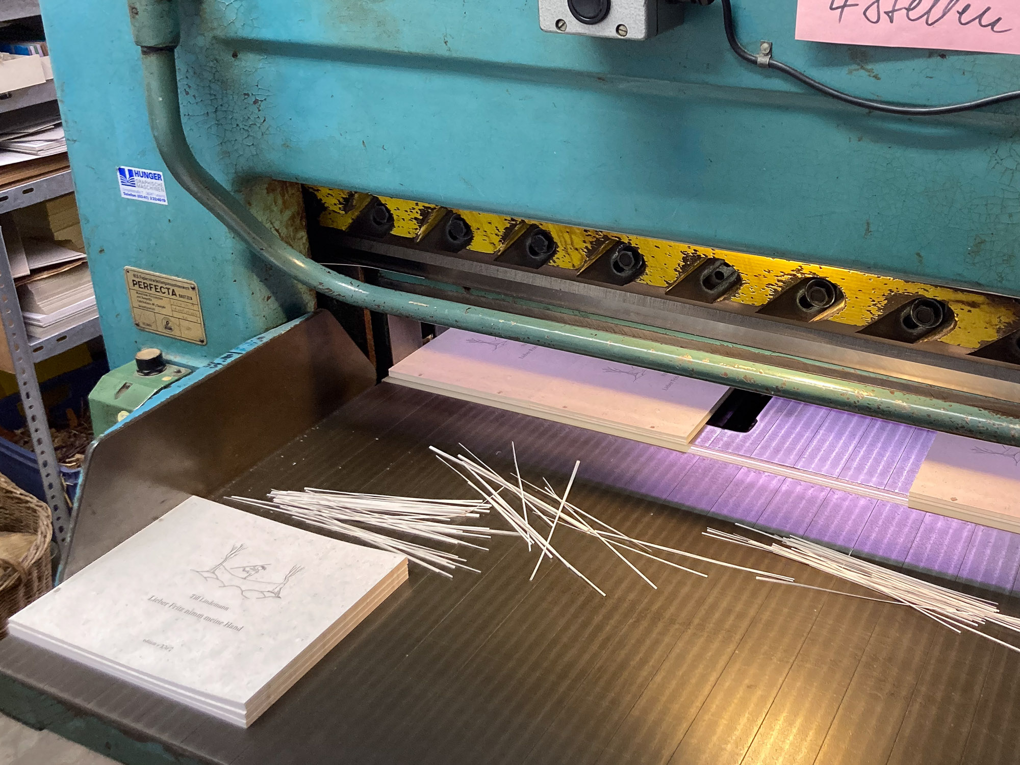Mehrere kleine Buchblock-Stapel und bereits abgeschnittene Papierstreifen liegen in der Aufnahme der historischen Schneidemaschine.