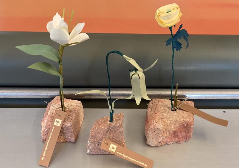 Gestecke bunter Papierblumen in kleinen Steinsockeln aus rotem Rochlitzer Porphyrtuff.